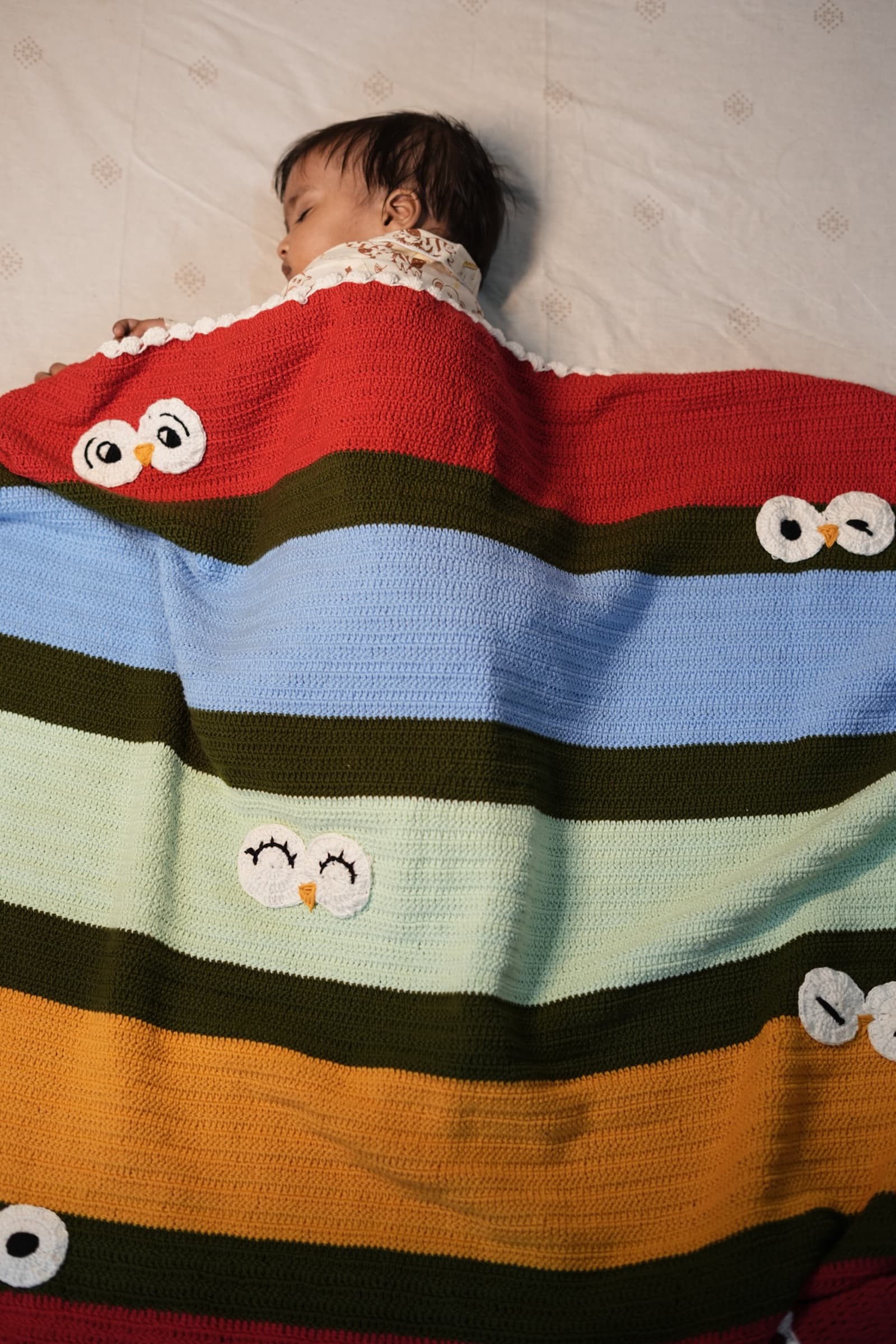 Dream Keeper striped crochet blanket with owl faces and tassels draped over a white chair